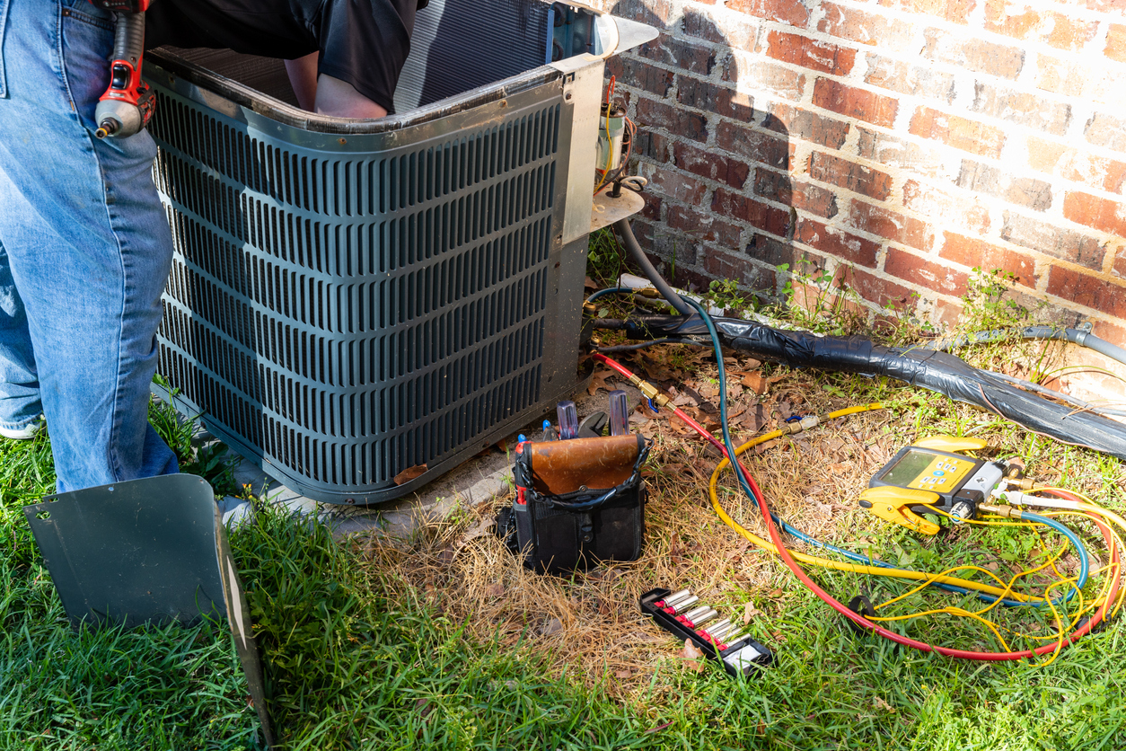 Air conditioner maintenance being performed on outdoor HVAC unit beside brick home