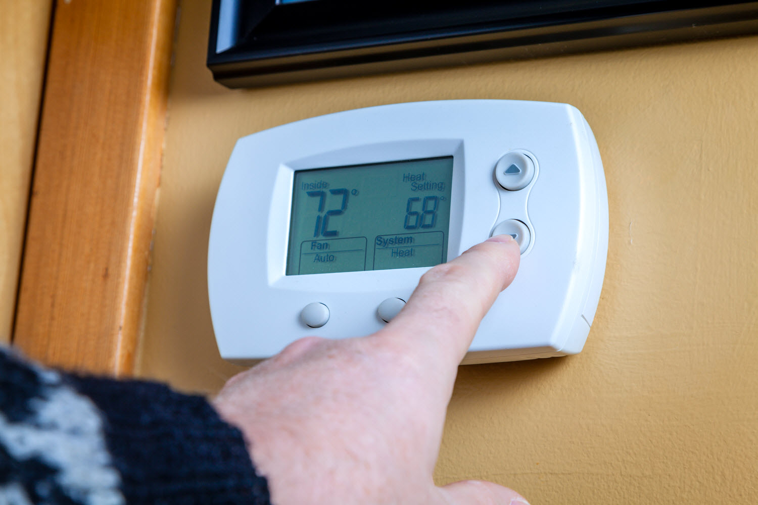 Hand lowering the temperature on a wall-mounted thermostat