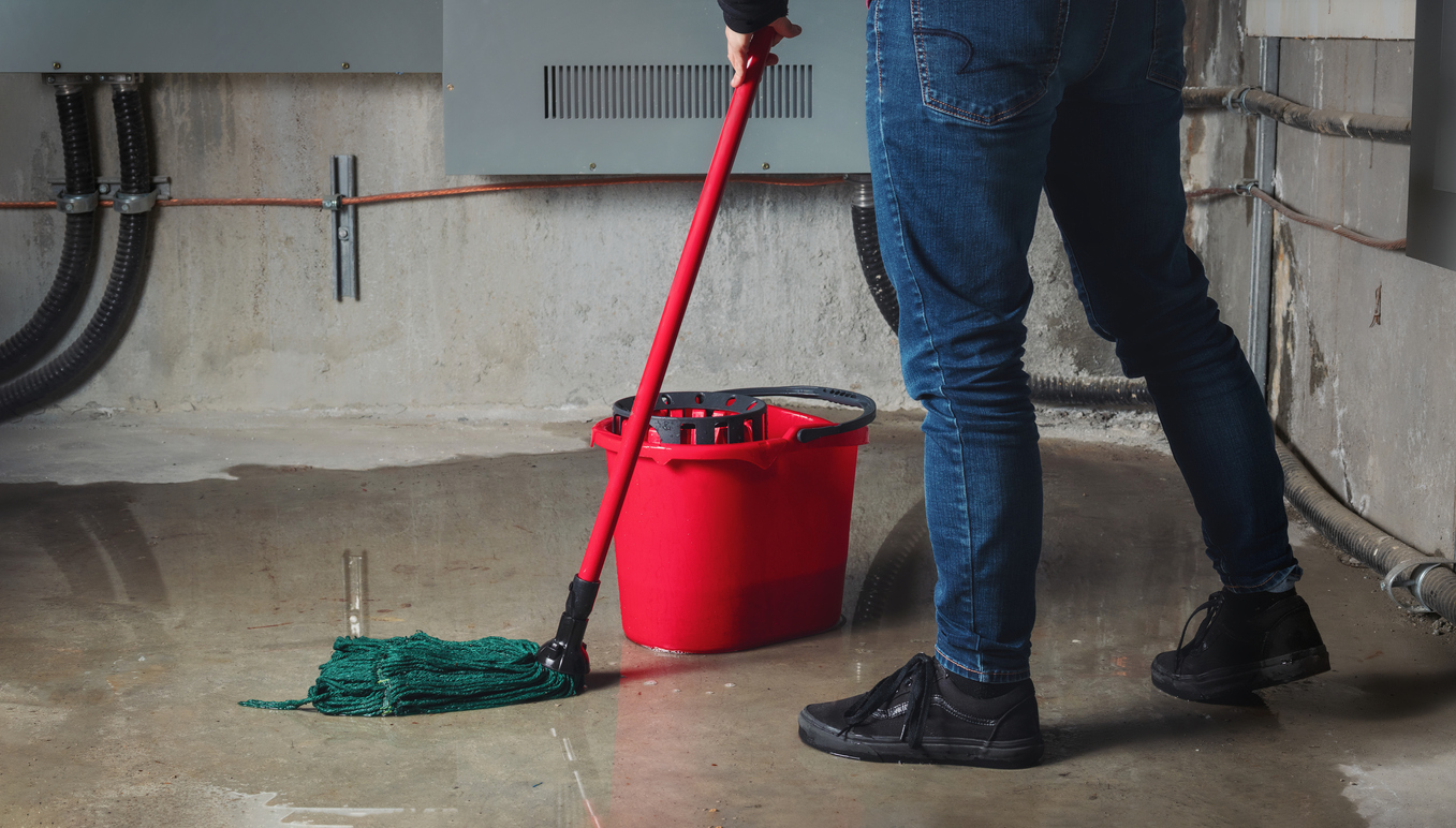 Person mopping flood water from water leaks in basement.