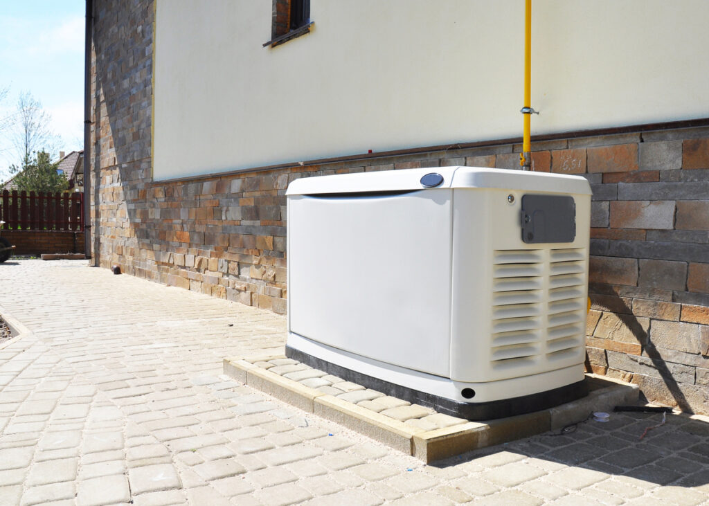 Residential generator installed outside of a white-stucco-and-brick home.