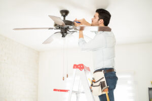 Electrician installing a ceiling fan while standing on a ladder