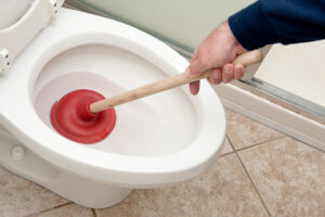 Plumber unclogging toilet with red plunger.