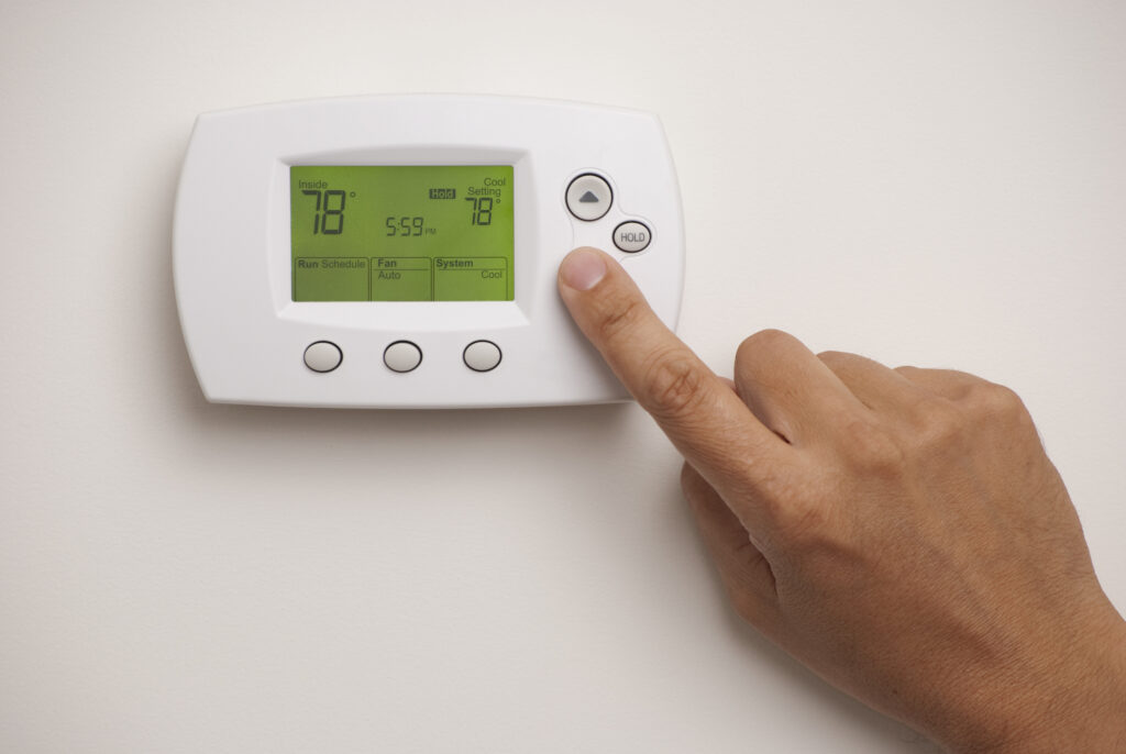 Hand adjusting programmable thermostat on a white wall. Digital screen shows 78 degrees.